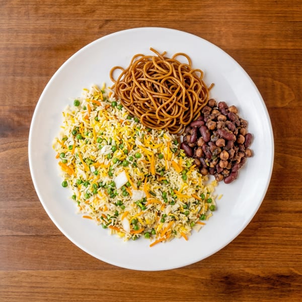 A white plate with vegetable fried rice, brown noodles, and dark red beans on a wooden table.