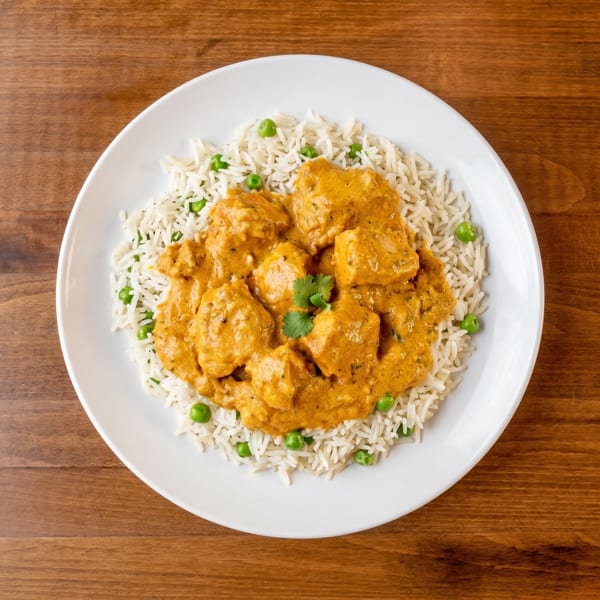 Overhead view of chicken tikka masala with basmati rice and green peas on a white plate.